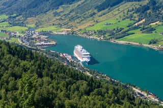 View from Huaren viewpoint in Olden, Norway, showing the Sky Princess cruise ship docked below surrounded by fjord waters, green valleys, and towering mountains