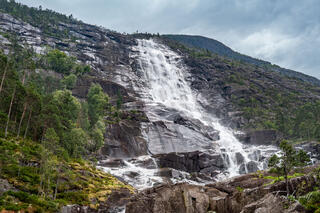 Langfoss Waterfall cascading down a steep granite mountainside in Haugesund, Norway, viewed from the base before starting the uphill hike.