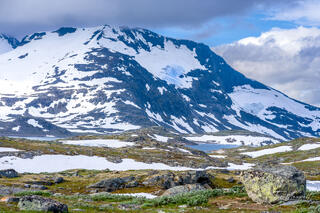 Snow-covered mountains and alpine tundra in the Sognefjellet mountain pass near Skjolden, Norway, with glacial ice visible in the distance under dramatic clouds