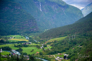 Mountain valley landscape near Skjolden, Norway with lush green fields, winding river, and distant waterfall cascading down steep cliffs