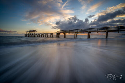 Fine-art photograph of Waimea Pier at sunset on Kauai’s west coast, with golden light reflecting on the ocean and long-exposure waves leading to the pier.