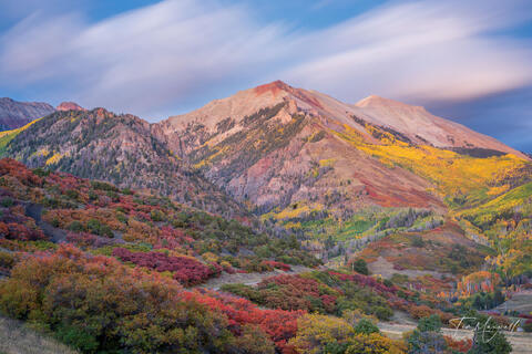 Fine art landscape photograph of the San Juan Mountains at sunset near Telluride, Colorado, featuring flowing clouds and vivid autumn colors in a long exposure.