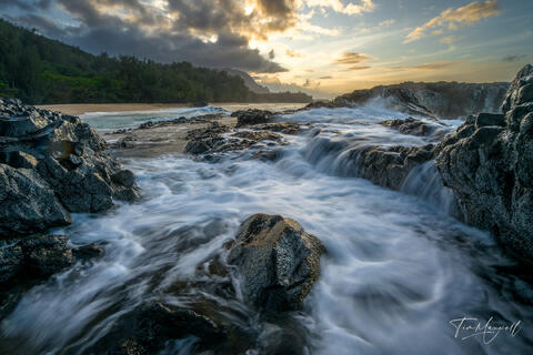 Fine-art photograph of waves cascading through volcanic rock at Lumahai Beach on Kauai during sunset, with glowing light and ocean motion.