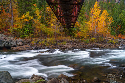 Fine art landscape photograph of the Wenatchee River in Tumwater Canyon, Washington, with autumn trees and a rustic iron bridge framed by golden foliage.